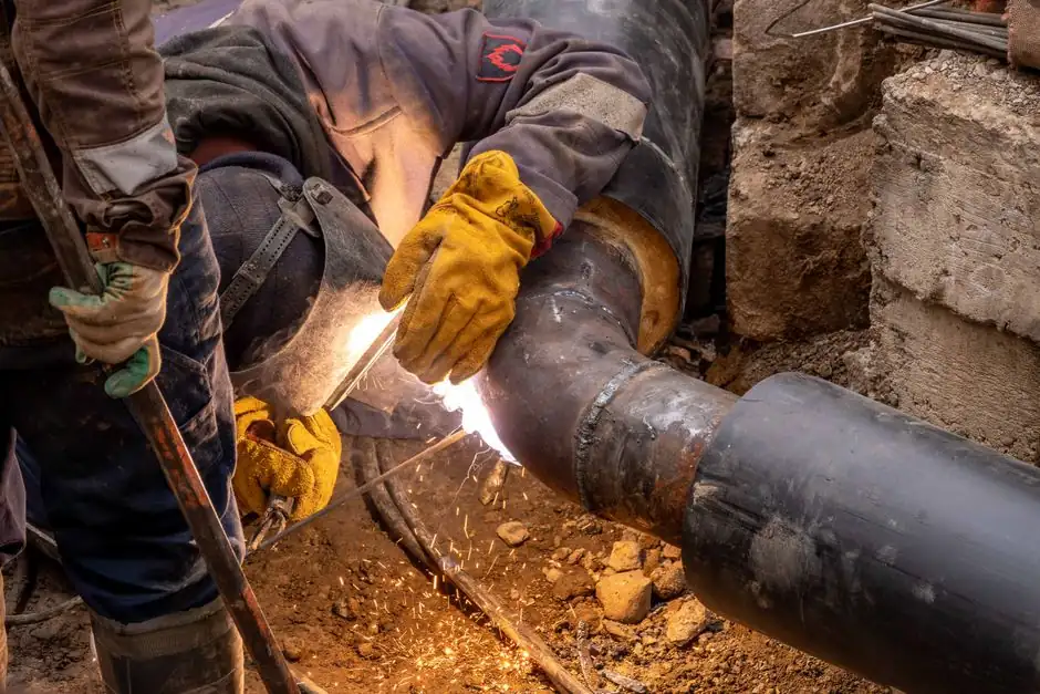 Close-up of a skilled worker welding steel pipes in an industrial setting, showcasing expertise and safety gear.