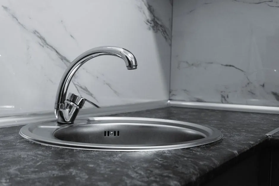 Stainless steel kitchen sink and faucet against marble backsplash in a modern kitchen.